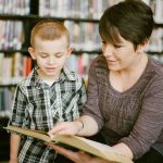 Giovane mamma con un libro in mano che insegna buoni comportamenti finanziari al suo bimbo