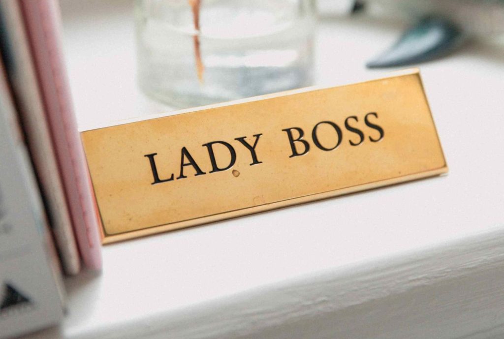 Targhetta dorata con scritto "Lady Boss" su una scrivania bianca accanto ad alcuni libri per ricordare che conquistare l'autonomia economica richiede un cambiamento di mentalità.
