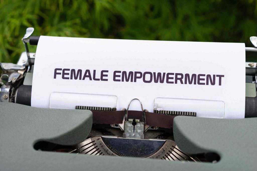 Dettaglio di una macchina da scrivere vintage grigia con un foglio con scritto "Female empowerment" cioè donne denaro ed emancipazione