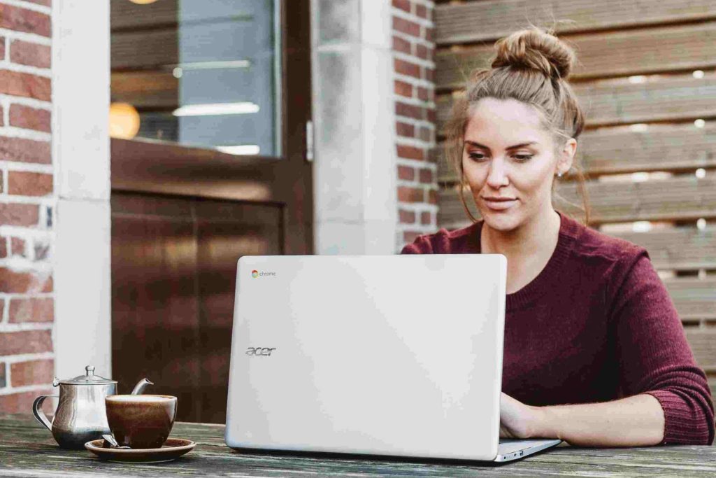 Giovane donna bionda in maglione bordò al computer con una tazza di te sul tavolo del giardino. Puoi creare il tuo fondo di emergenza usando fogli excel