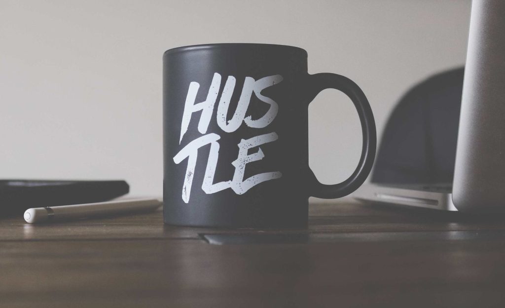 tazza scura con scritto "Hustle" su una scrivania: Creare un'attività che genera un'entrata extra per gestire lo stress da debito