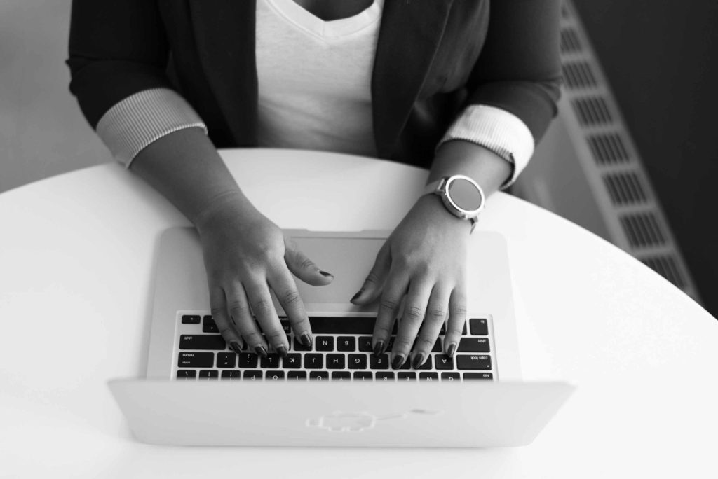 Immagine in bianco e nero di donna che lavora al computer su una scrivania bianca per investire su te stessa: