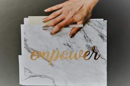 cartello bianco marmorizzato con scritta oro "Empower" e mano di donna che lo sorregge