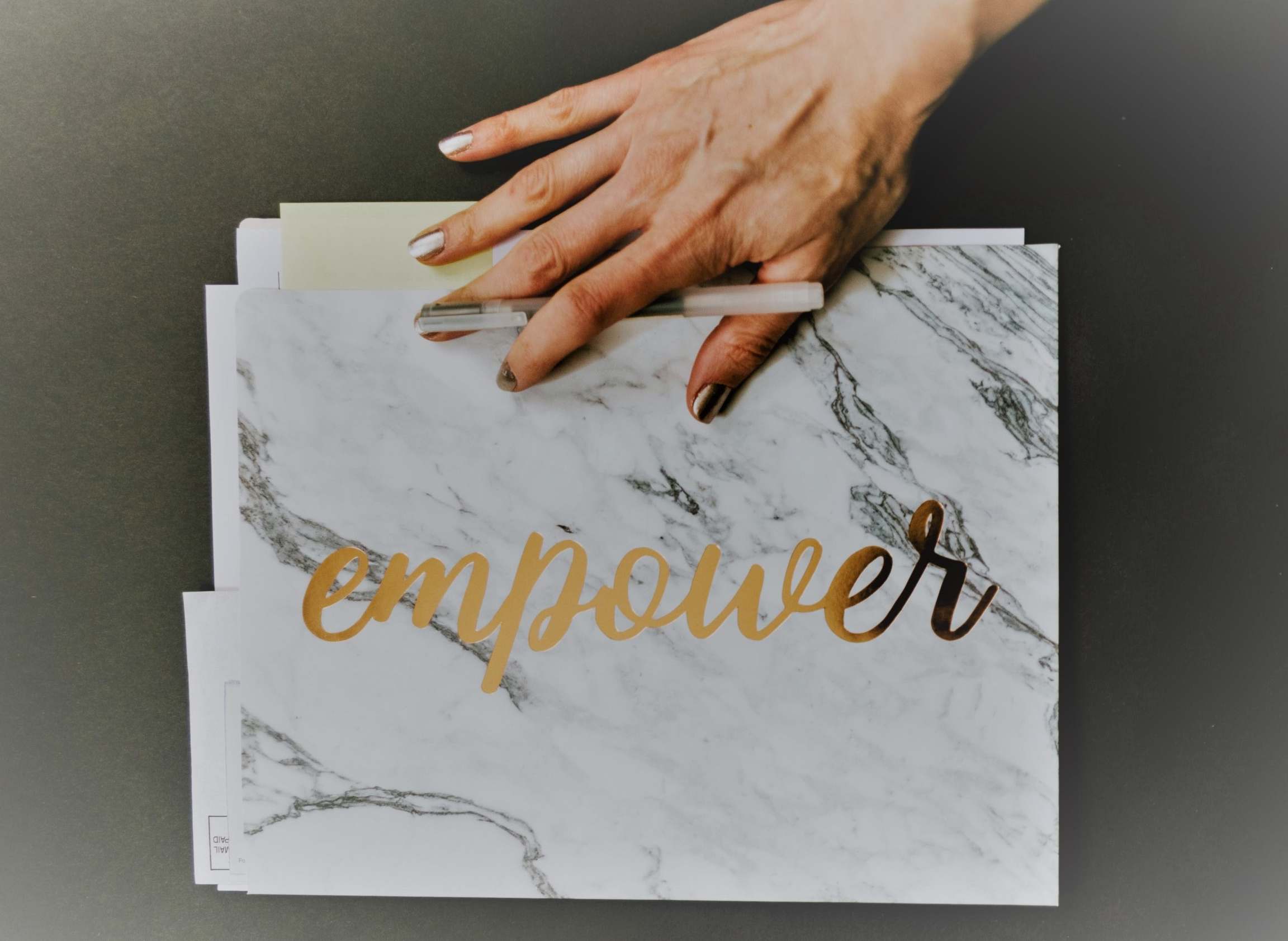 cartello bianco marmorizzato con scritta oro "Empower" e mano di donna che lo sorregge