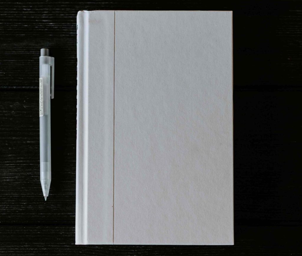 Notebook e penna, bianchi, su un tavolo di legno molto scuro: prima di creare la tua vision board accertati di ascoltarti e annotare tutte le idee sul tuo notes preferito