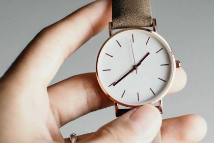 Ottimizzare la giornata: mano femminile che regge un orologio con quadrante bianco, dettagli rose gold e cinturino beige