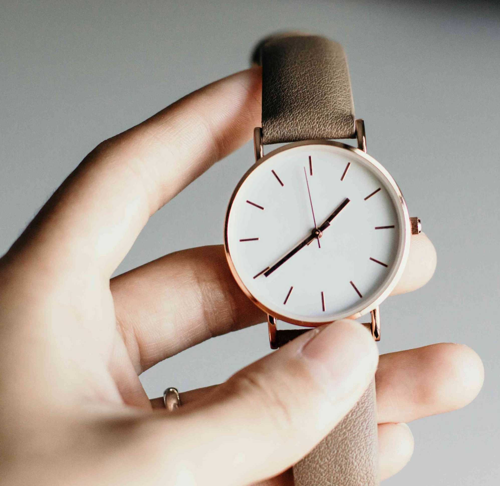 Ottimizzare la giornata: mano femminile che regge un orologio con quadrante bianco, dettagli rose gold e cinturino beige