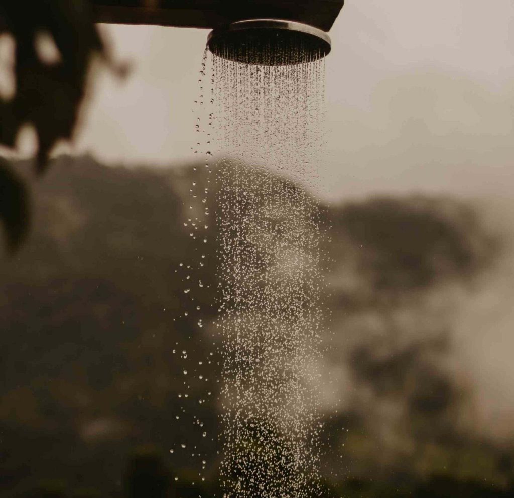 Getto d'acqua di una doccia fra le piante con un magnifico panorama di campagna sullo sfondo