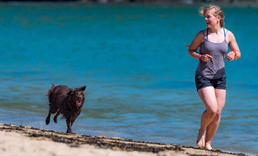 immagine di donna in calzoncini e canottiera che corre sulla spiaggia con il suo cane nero: che tipo di risparmiatrice sei? Una maratoneta?