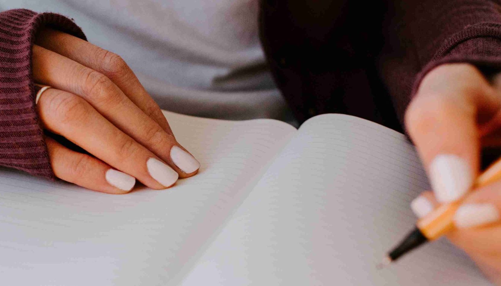 Dettaglio di mani di donna con smalto bianco che scrive su un quaderno con un pennarello fineliner nero che cosa inserire nel suo budget