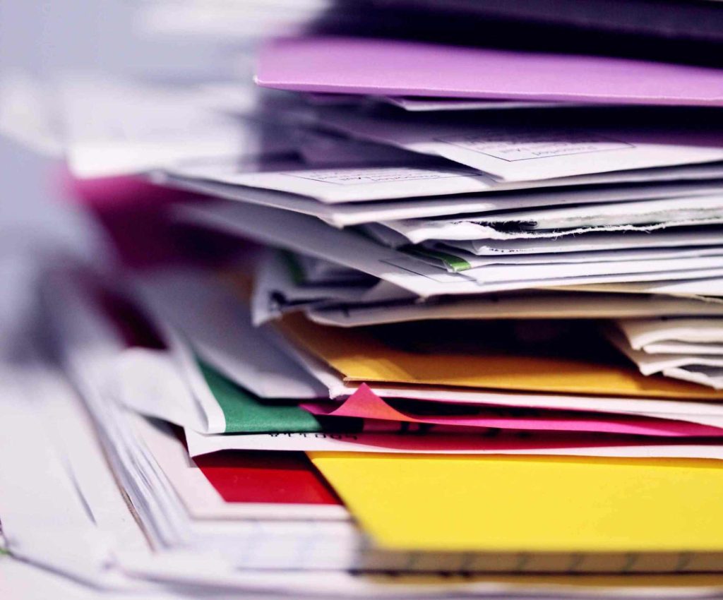 Pila di cartelline colorate e documenti disordinati su sfondo chiaro: fare decluttering e riorganizzare i documenti ti aiuta a risparmiare tempo e denaro