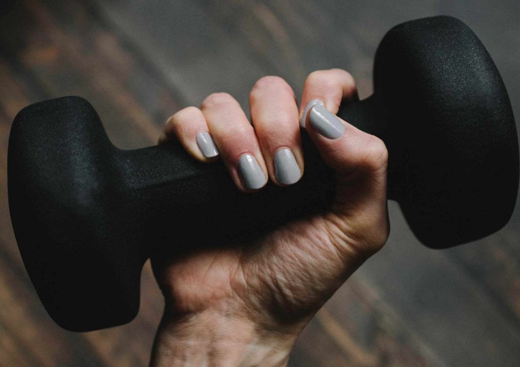 Dettaglio di mano di donna con smalto grigio che si allena con un piccolo peso nero. Anche l'intelligenza finanziaria deve essere allenata