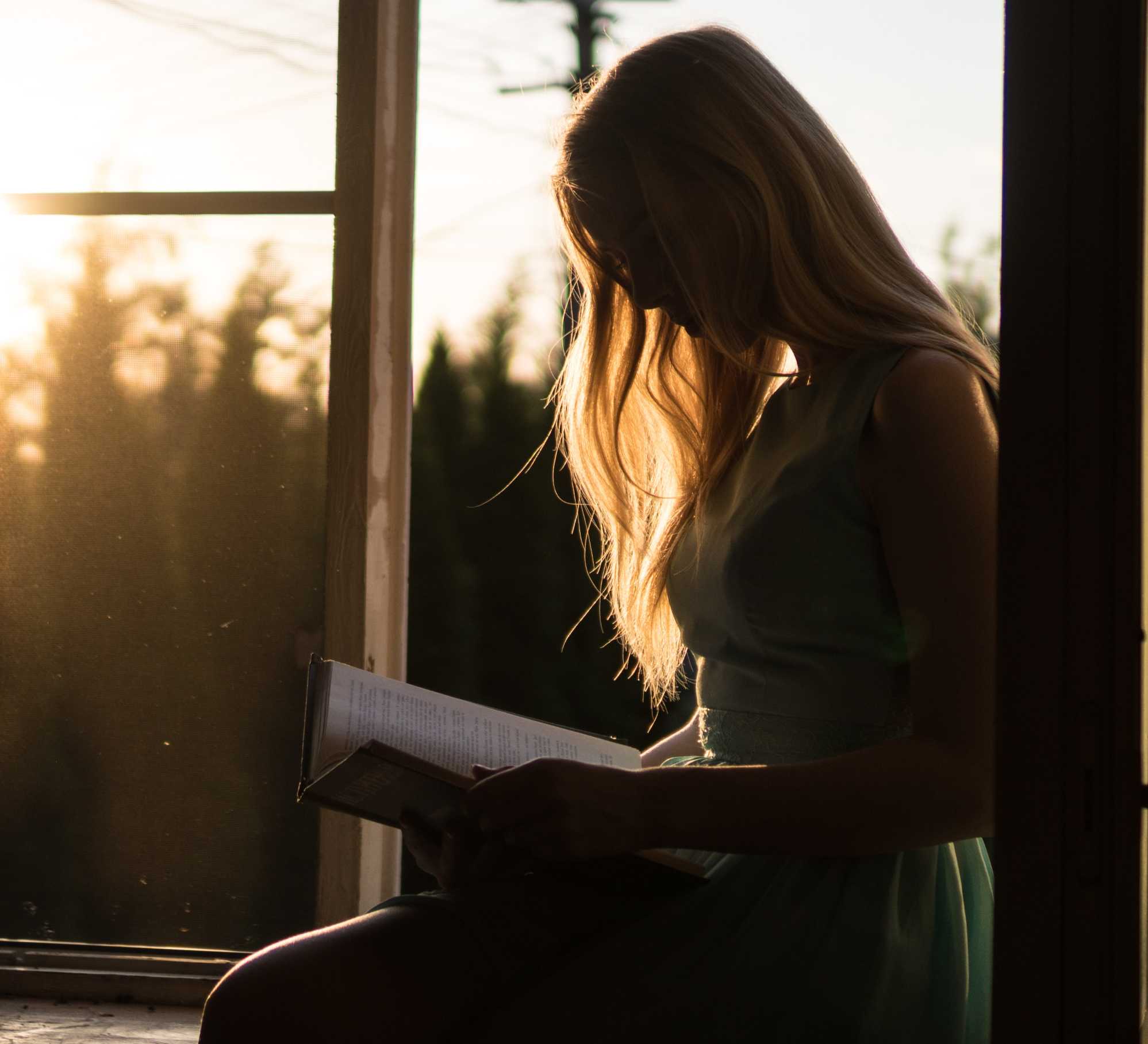 Immagine di donna in penombra alla finestra che legge un sera d'estate