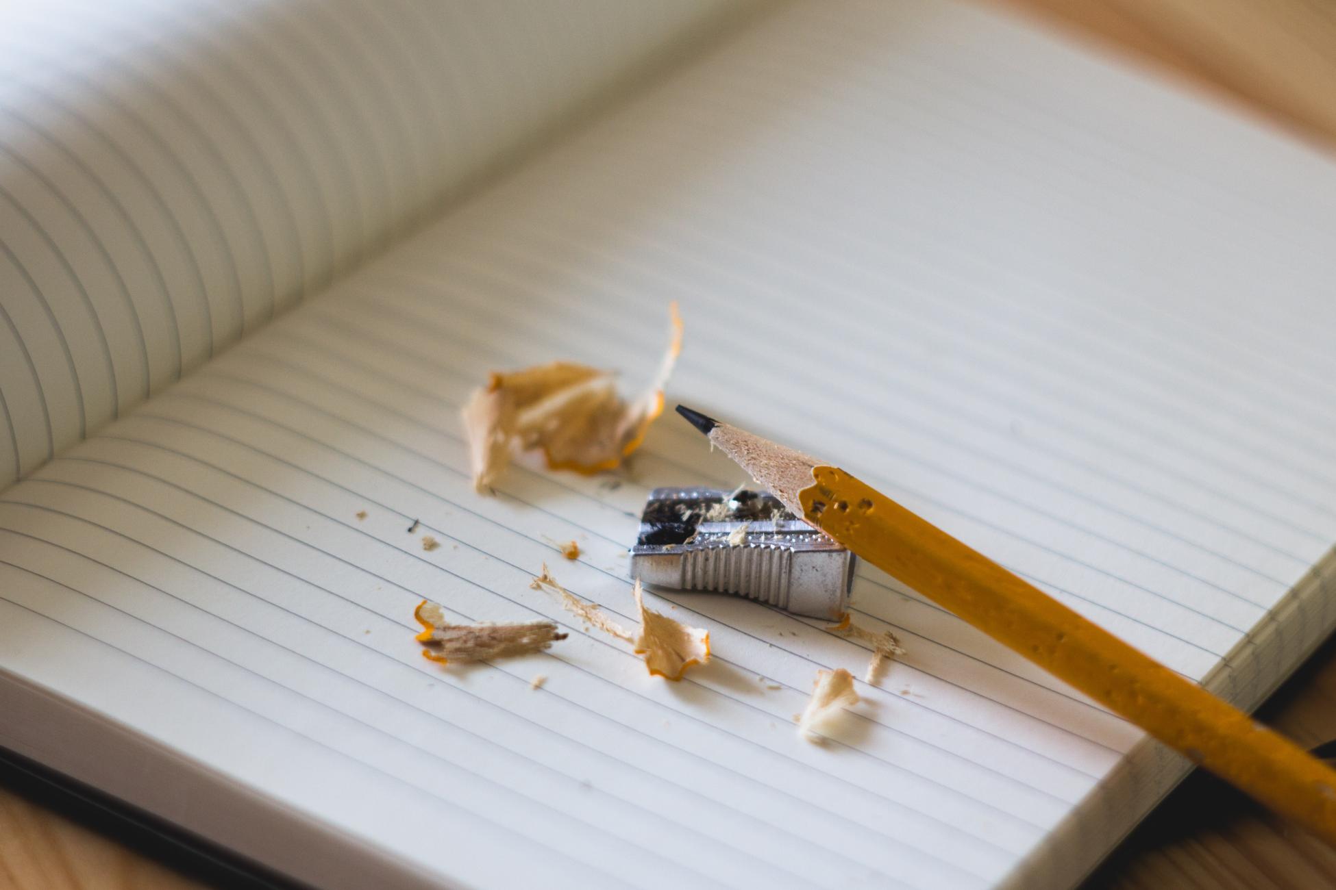Dettaglio di un taccuino con pagine a righe con matita ben temperata e un temperino in metallo, gli strumenti per iniziare a scrivere un diario